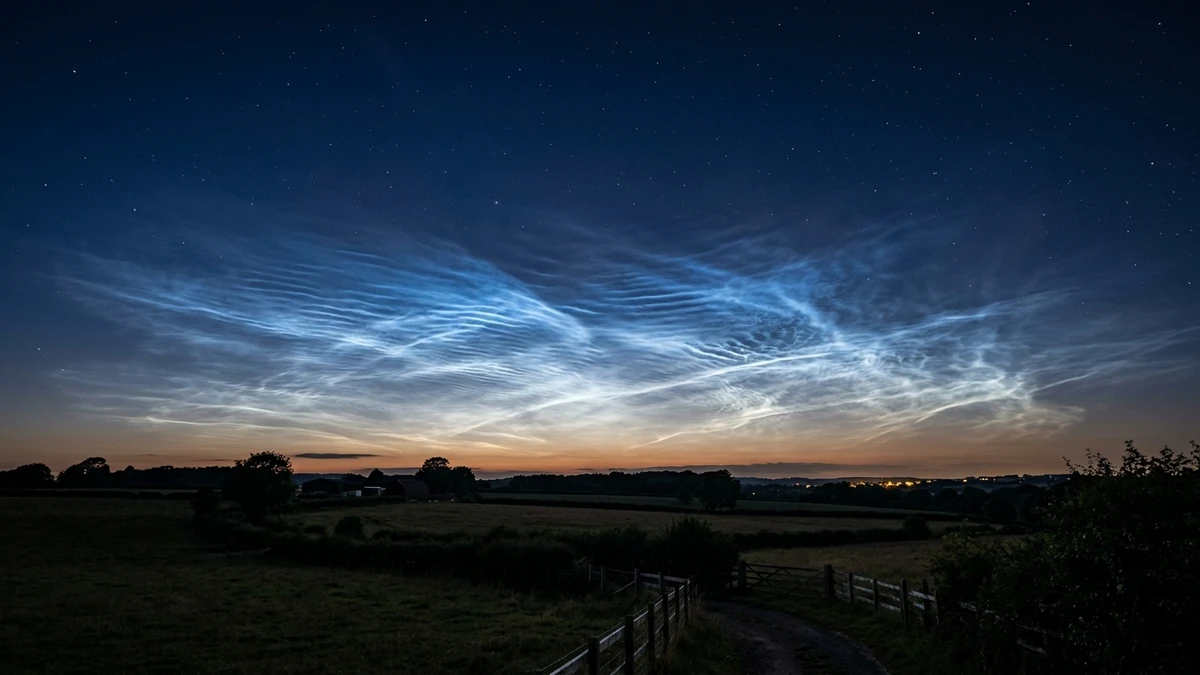 Noctilucent clouds glowing electric blue and silver on the northern horizon after sunset, above silhouetted fields